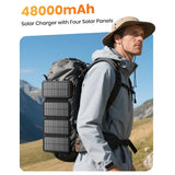 Hiker charging the 48000mAh solar power bank with four solar panels unfolded and hanging from a backpack
